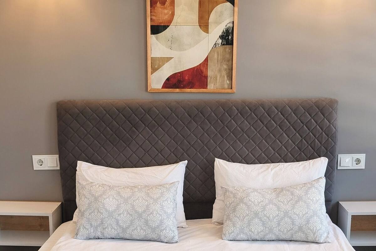 A double bed with a quilted headboard, two bedside lamps, and a framed abstract painting on the wall.