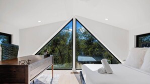 A modern bedroom with a large window, a wooden bench, and a bed with white bedding. - Walkable Lady Bird East ATX Home for 8 | Near Chavez, Nightlife, Trails & More (Austin)