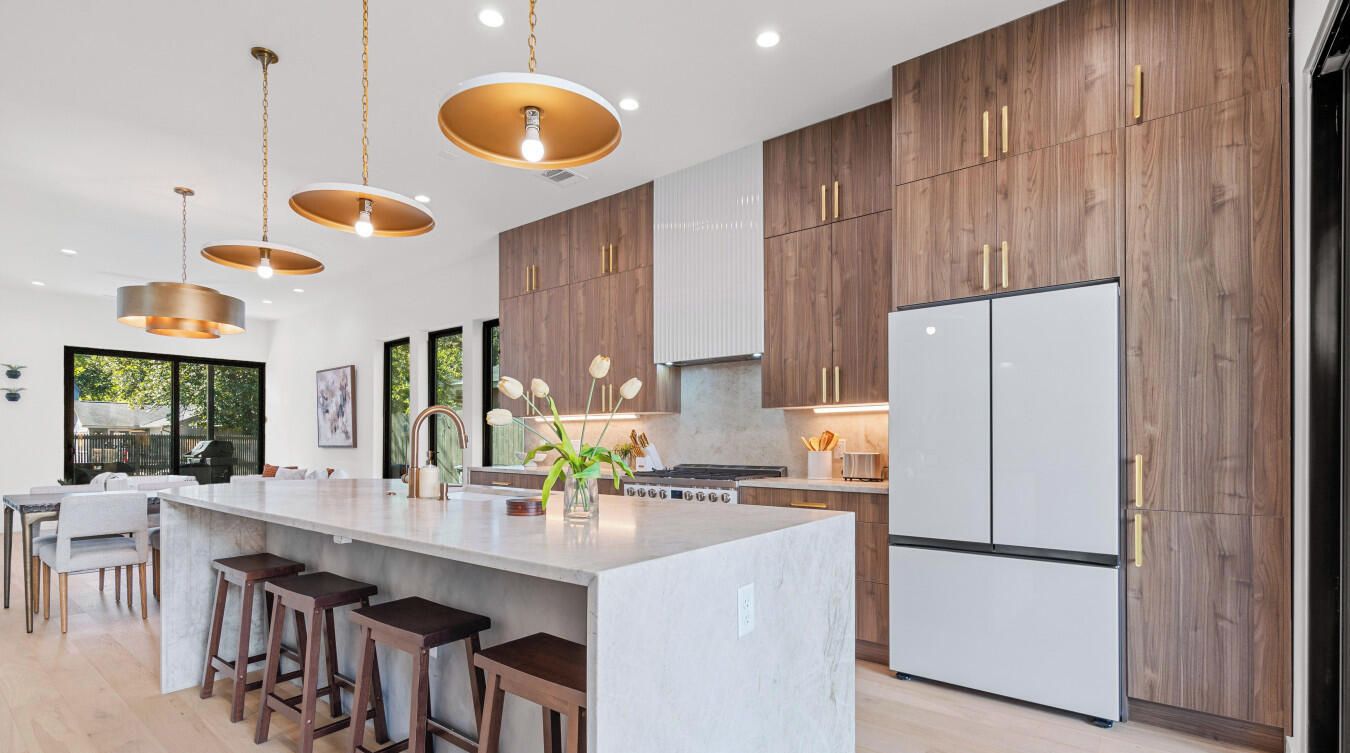 A modern kitchen with a central island, wooden cabinets, and pendant lighting.