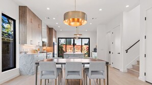 A modern kitchen with a large island, wooden cabinets, and a dining area with a marble countertop and grey chairs. - Walkable Lady Bird East ATX Home for 8 | Near Chavez, Nightlife, Trails & More (Austin)