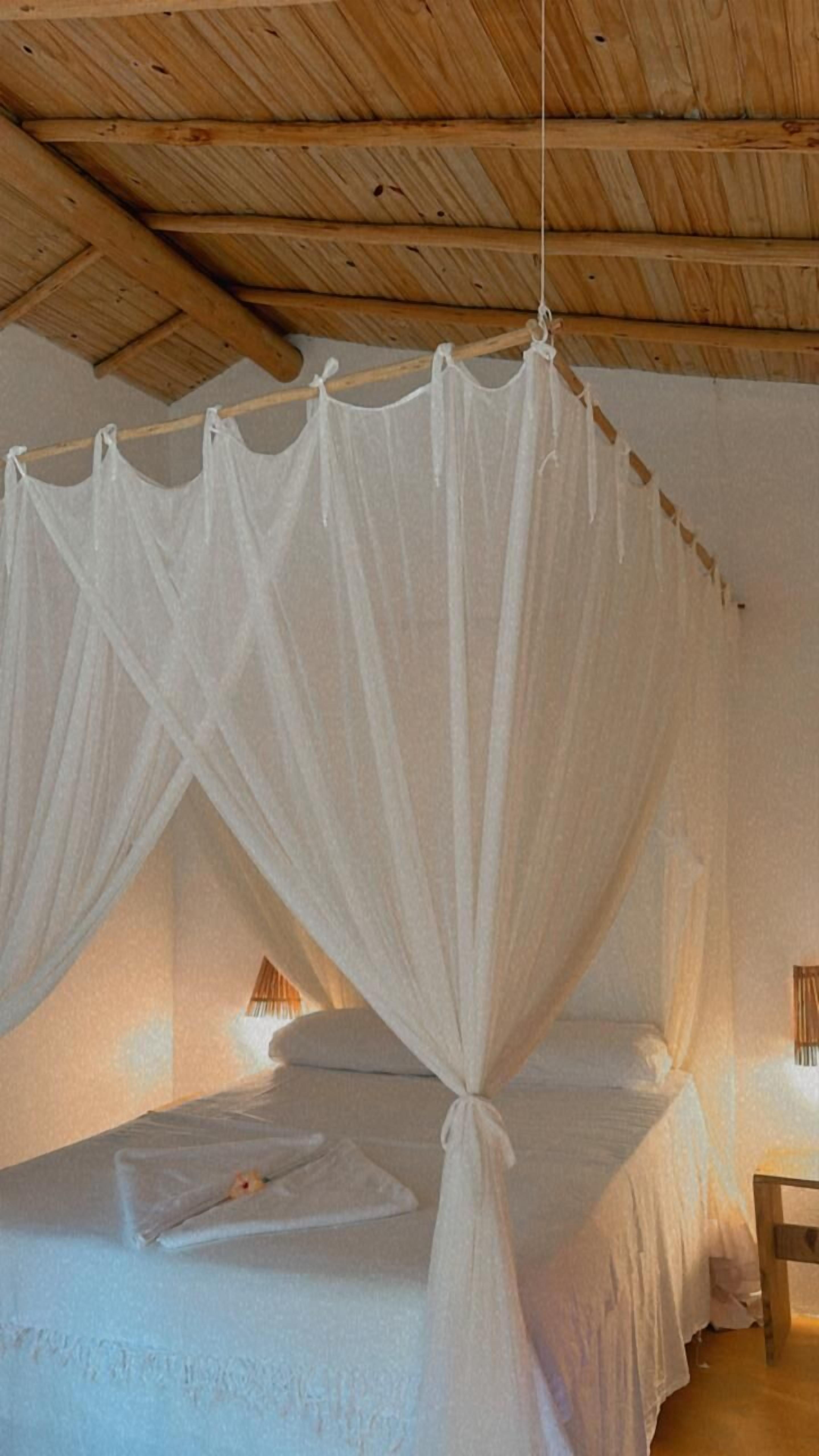 Un dormitorio con cama con dosel, vigas de madera en el techo y lámparas de noche.