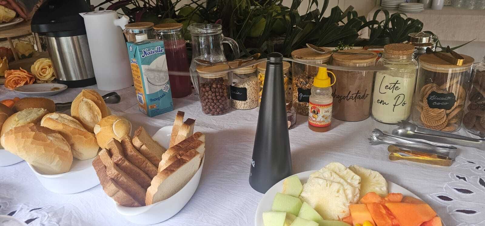 Une table sur laquelle on trouve divers aliments, notamment du pain, des fruits et des pots de condiments.