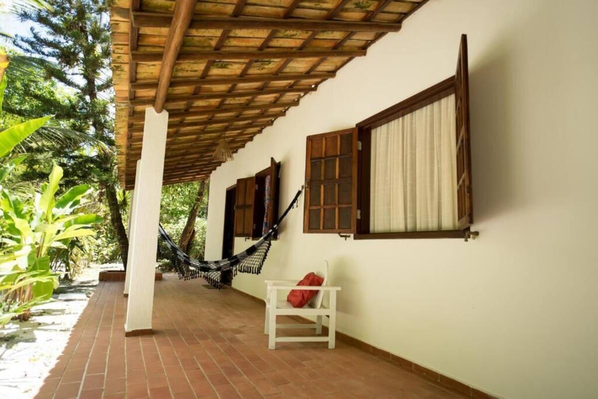 A covered patio with a hammock, a white chair, and a window with wooden shutters.