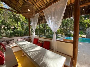 A covered outdoor seating area with a pool in the background. - Vila Flor da Mata (Porto Seguro)