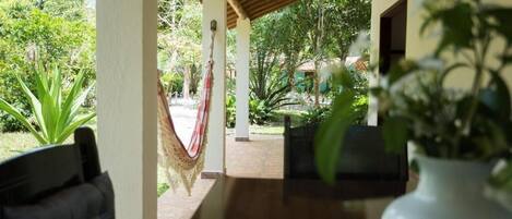 A covered outdoor area with a wooden table and chairs, a hammock, and potted plants.