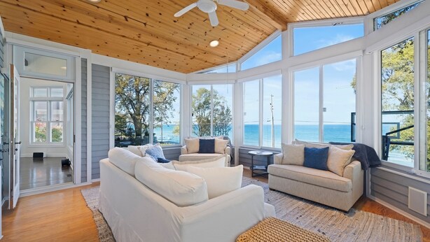 A spacious sunroom with a wooden ceiling, large windows, and a view of the ocean. - Lake Shore Living - lakefront, pool, sleeps 16 (New Buffalo)