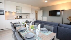 A modern kitchen with white cabinets, a built-in oven, and a dining area with grey chairs and a wooden table set for six.