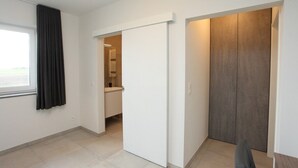 A modern, minimalist room with a sliding door, a window with curtains, and a view of a hallway.