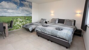 A bedroom with a large bed, two bedside tables, a desk with chairs, and a mural of a field and sky.