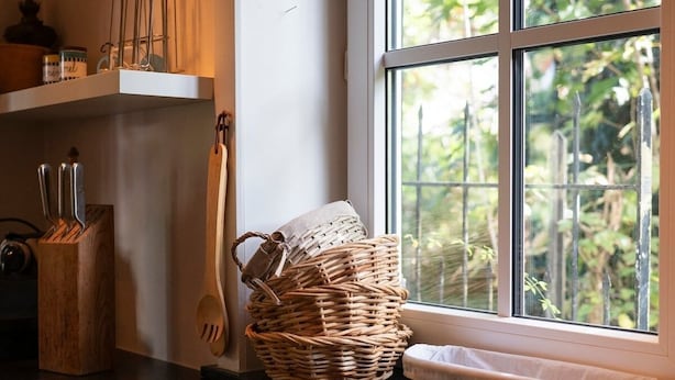 A kitchen counter with a woven basket, a wooden knife block, and a window with a view of greenery.