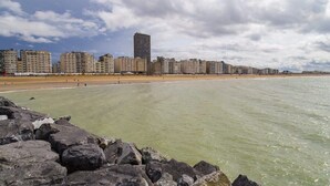 A beach with a rocky foreground, a sandy shore, and a row of high-rise buildings in the background.
