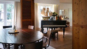 A dining area with a wooden table, chairs, a grand piano, and a ship model.