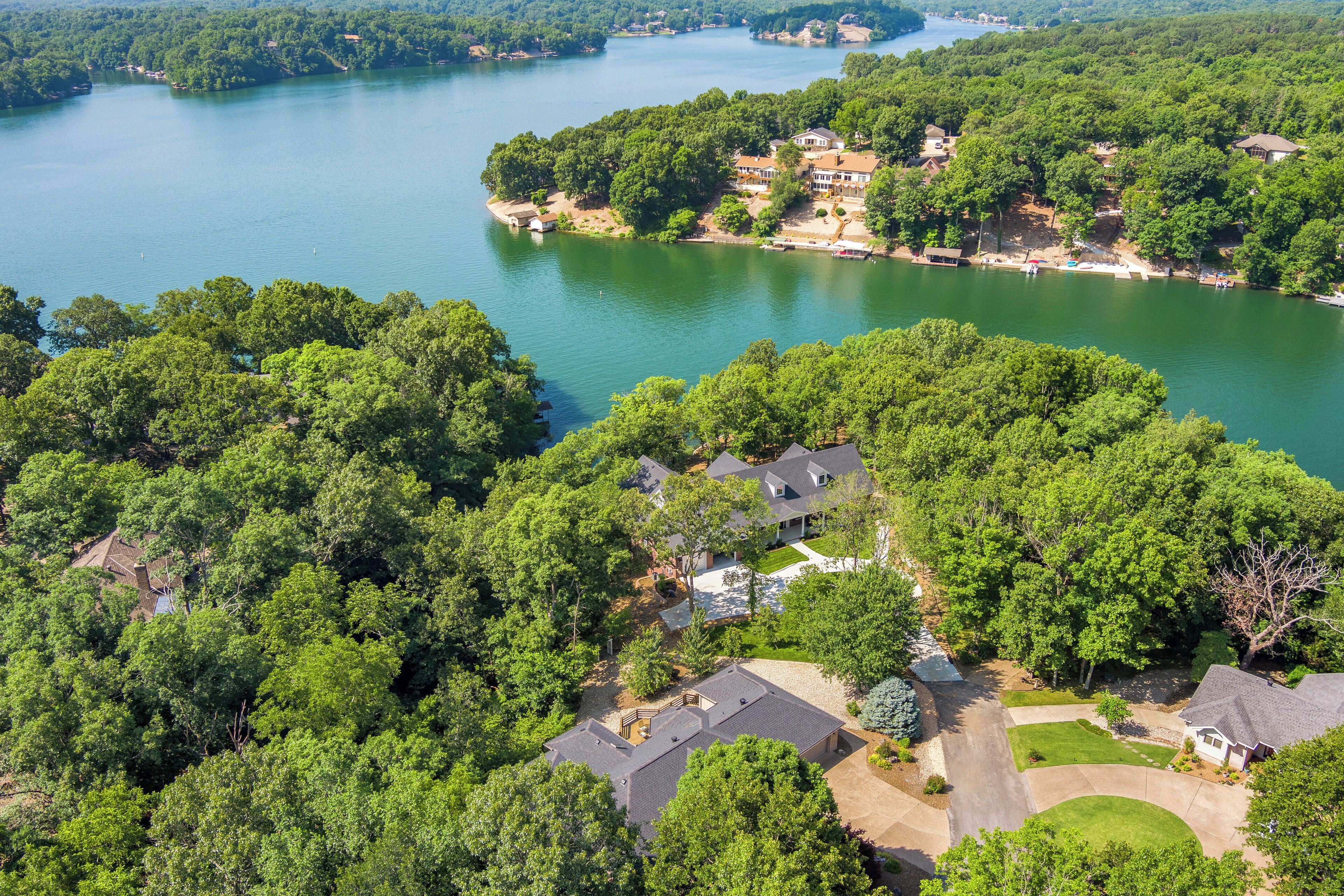 An aerial view of a residential area with houses surrounded by dense greenery and a large body of water.