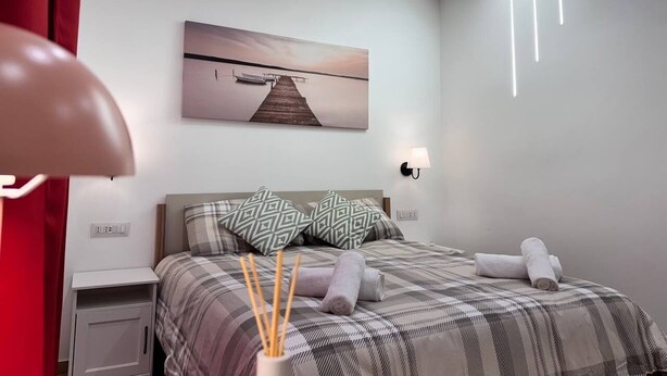 Een moderne slaapkamer met een bed, een nachtkastje, een wandlamp en een schilderij van een steiger.