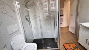 Een moderne badkamer met een douchecabine van glas, een wit toilet en een houten vloer.
