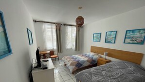 Quarto de hotel com duas camas, uma escrivaninha com computador, uma cadeira e um pequeno frigorífico.