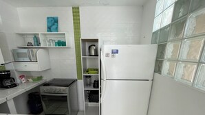 Cozinha compacta com armários brancos, micro-ondas, chaleira e geladeira.