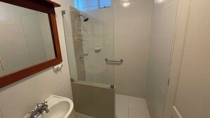 Casa de banho com cabine de duche em vidro, lavatório branco com torneira antiga e espelho com moldura de madeira.