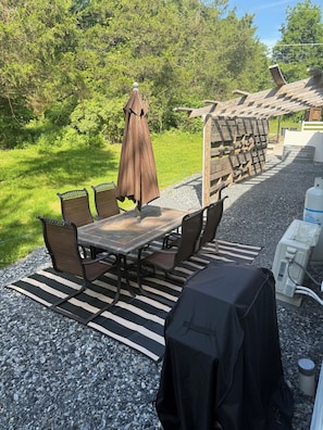 An outdoor patio with a table and chairs, a grill, and a covered area. - Charming farmhouse-style apartment, nestled in a peaceful, quiet area of PA. (Wellsville)