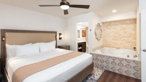A hotel room with a large bed, a ceiling fan, a bathroom with a bathtub, and a patterned rug.