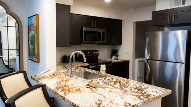 A modern kitchen with dark cabinets, stainless steel appliances, a marble countertop, and a built-in sink.