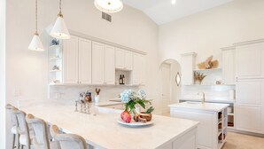 Una cocina moderna con una isla grande, armarios blancos e iluminación colgante.