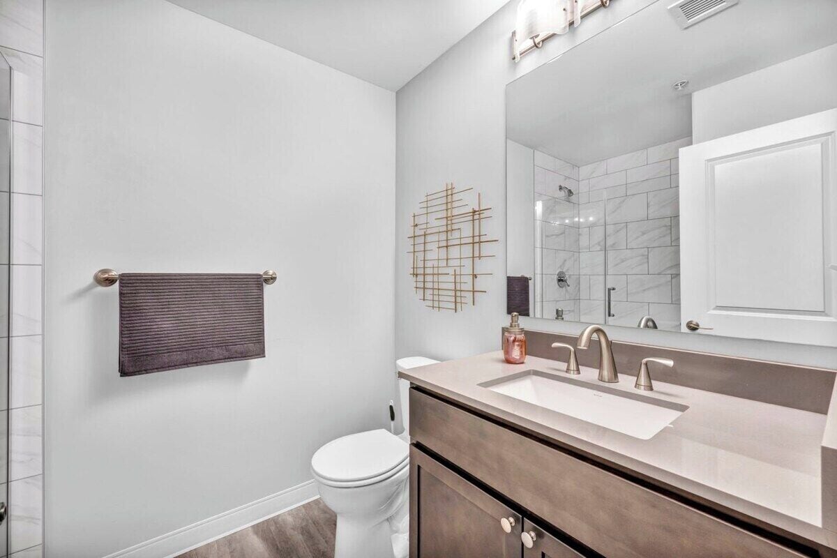 A modern bathroom with a white toilet, a vanity with a large mirror, and a towel rack.