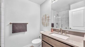 A modern bathroom with a white toilet, a vanity with a large mirror, and a towel rack.