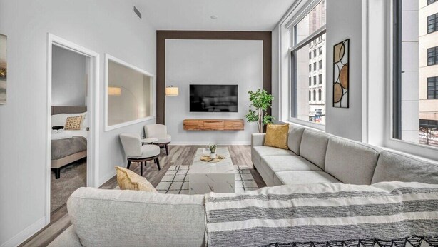 Ein modernes Wohnzimmer mit einer großen Couch, einem Couchtisch und einem an der Wand montierten Fernseher.