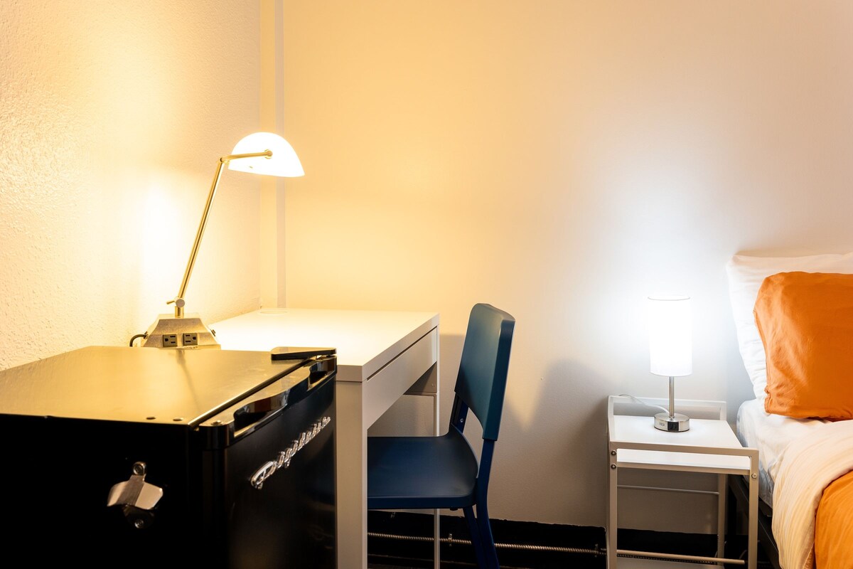 Ein Hotelzimmer mit Schreibtisch, Stuhl und Nachttisch mit Lampe.