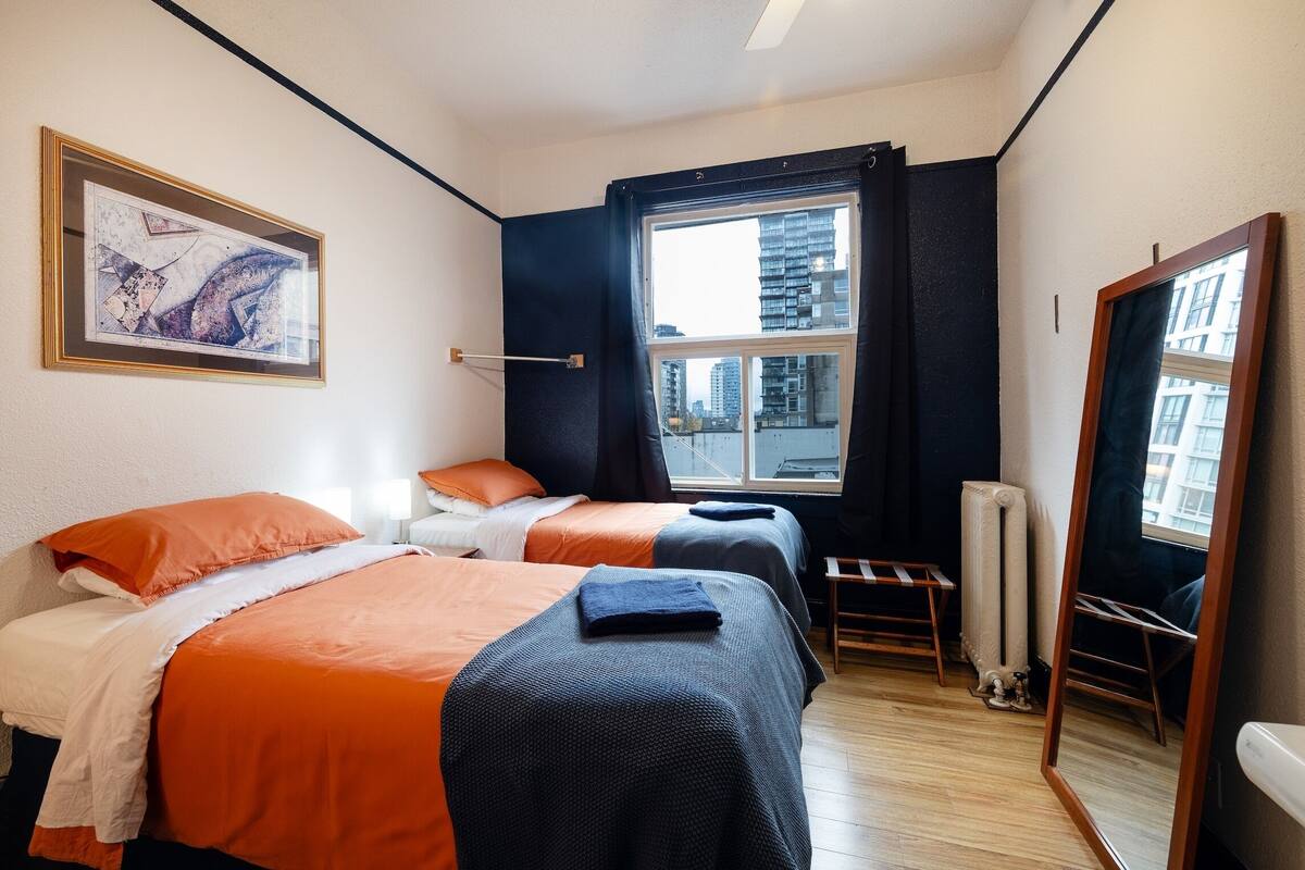 Een hotelkamer met twee bedden, een groot raam, een radiator en een spiegel.