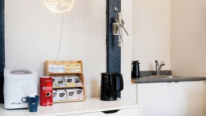 Una cocina con cafetera, taza de café, exhibición de granos de café y un lavamanos.