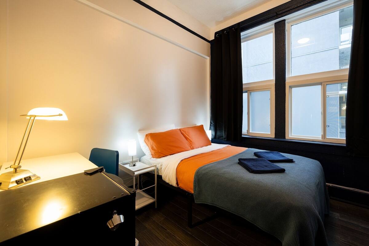 Een hotelkamer met een bed, een bureau met lamp, een stoel en een raam met gordijnen.