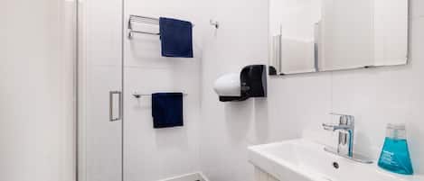 A modern bathroom with a glass shower enclosure, two towels, a hand dryer, and a sink with a mirror above it.