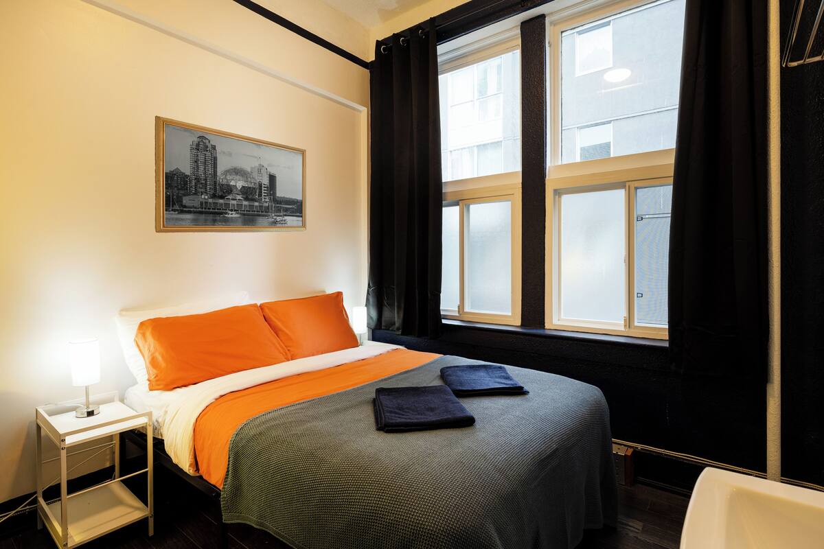 Een hotelkamer met een bed, nachtkastje, raam met gordijnen en een ingelijst foto aan de muur.