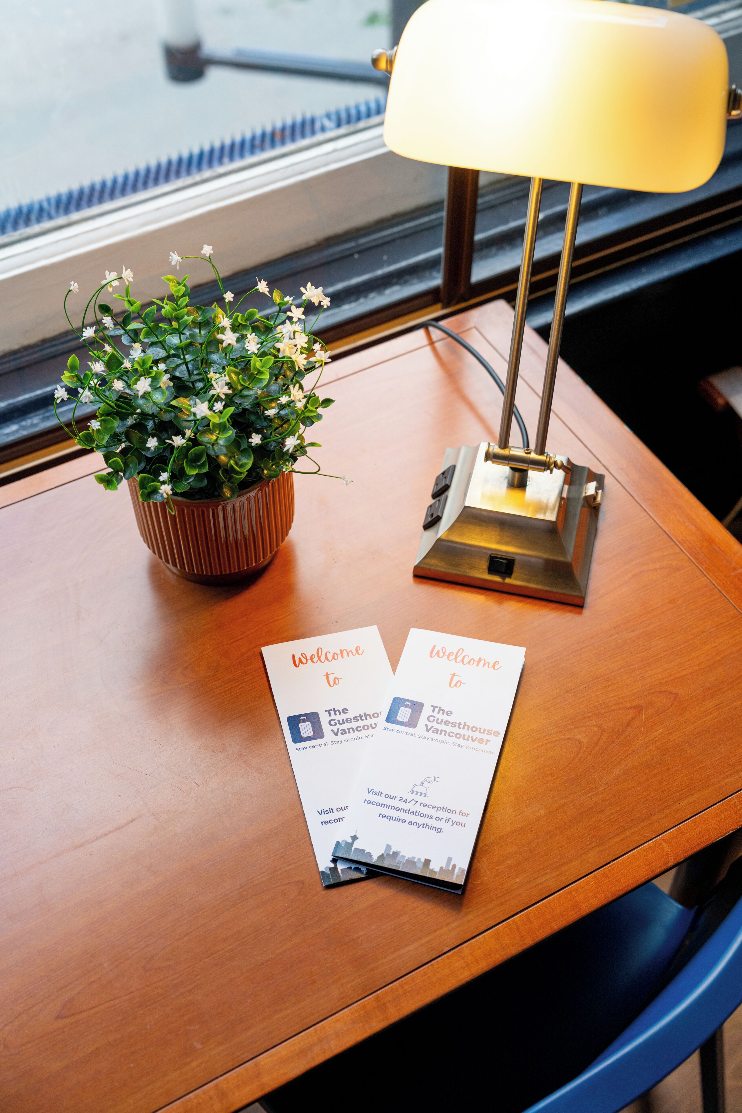 A wooden table with a potted plant, a lamp, and a welcome brochure.