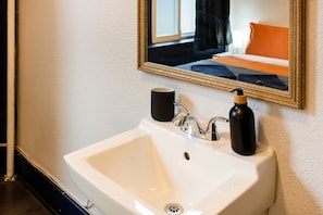 A white bathroom sink with a mirror above it, a black soap dispenser, and a black cup on the sink. - The Guesthouse Vancouver Downtown (Vancouver)
