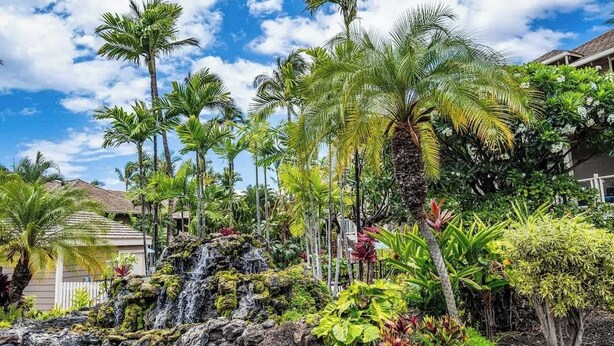 Un jardín tropical con una cascada, palmeras y diversas plantas.
