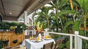 Un área de comedor al aire libre con una mesa dispuesta para el desayuno, rodeada de exuberante vegetación tropical y una valla de madera.