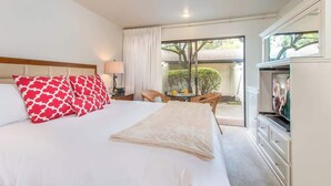 Una habitación de hotel con una cama grande, un televisor, un escritorio con lámpara y vistas al exterior.