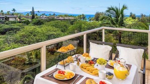 A breakfast setup on a balcony with a scenic view of the ocean and greenery. - Oceanview Retreat Walk to Beach & Restaurants (Kihei)