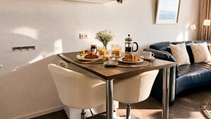 Een eethoek met een ontbijt gedekte tafel, een koffiezetapparaat en een bank op de achtergrond.