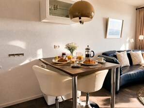 Un coin repas avec une table mise pour le petit-déjeuner, une machine à café et un canapé en arrière-plan.
