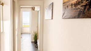 Een hal met uitzicht op een balkon, een schilderij aan de muur en een bloempot.