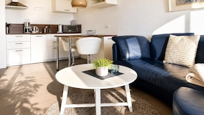 Een moderne woonkamer met een bank, salontafel en een eethoek, met een keuken op de achtergrond.