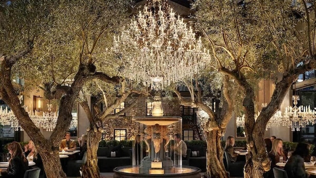 An outdoor dining area with a central fountain, surrounded by trees and illuminated by chandeliers. - Luxe Golf View Condo | Prime Napa Location (Napa)