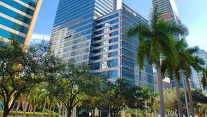 A high-rise building with a modern glass facade, surrounded by palm trees and other buildings. - Luxury Four Seasons Condo | Free Valet & Gym (Miami)
