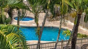 A pool surrounded by palm trees and a white fence. - Beach Retreat | Walk to Maui’s Best Shores (Kihei)