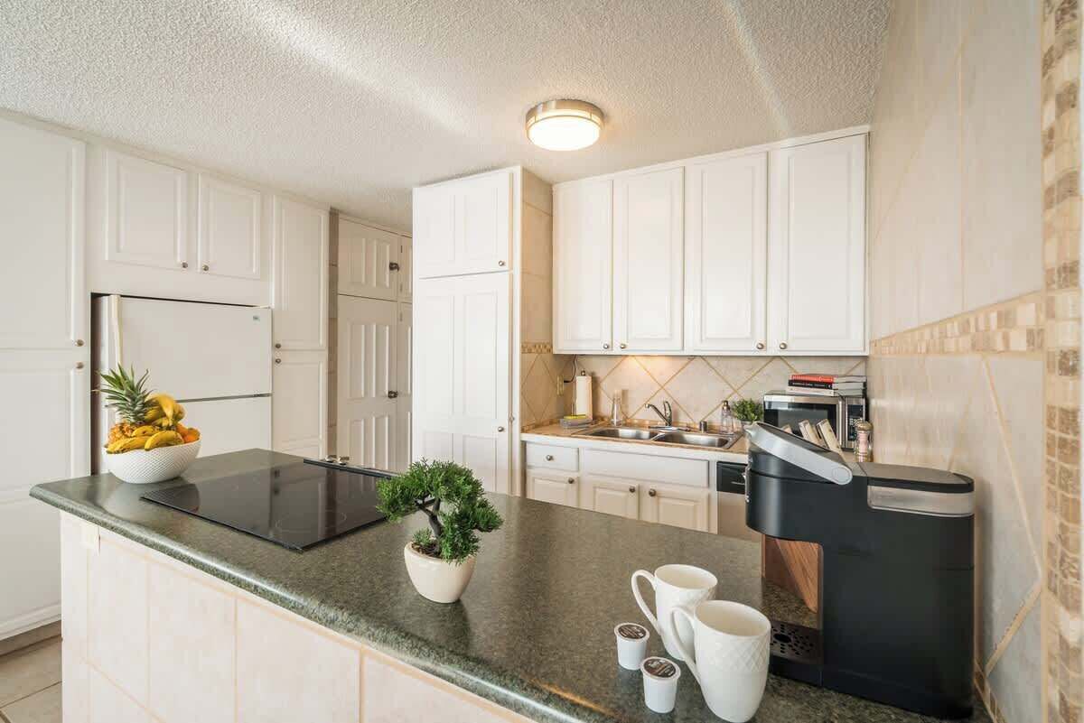 A modern kitchen with white cabinets, a black countertop, a built-in stove, and a coffee machine.