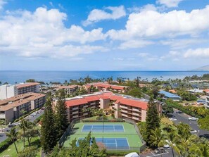 Ein Resort mit mehreren Gebäuden, einem Tennisplatz und Blick auf den Ozean.